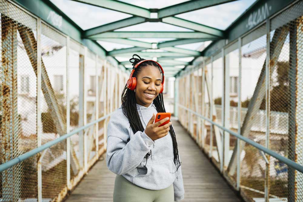 young woman outside looking at phone wearing headphones