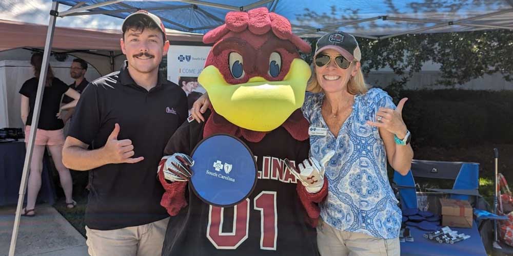 man and woman standing with university cocky mascot holding blue cross sign