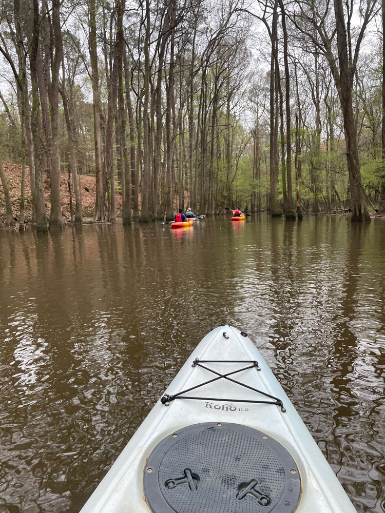 front of kayak on river with other boats down the river
