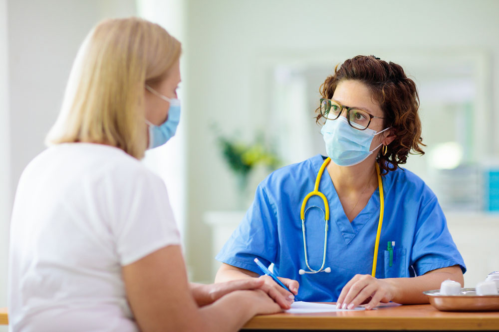 doctor in blue scrubs with stethoscope talking with woman 