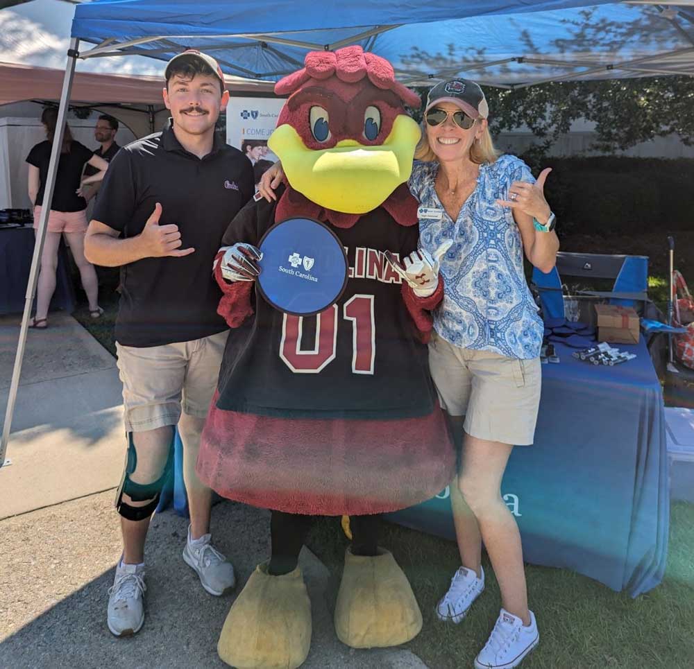 man and woman pose with Cocky mascot holding Blue Cross sign