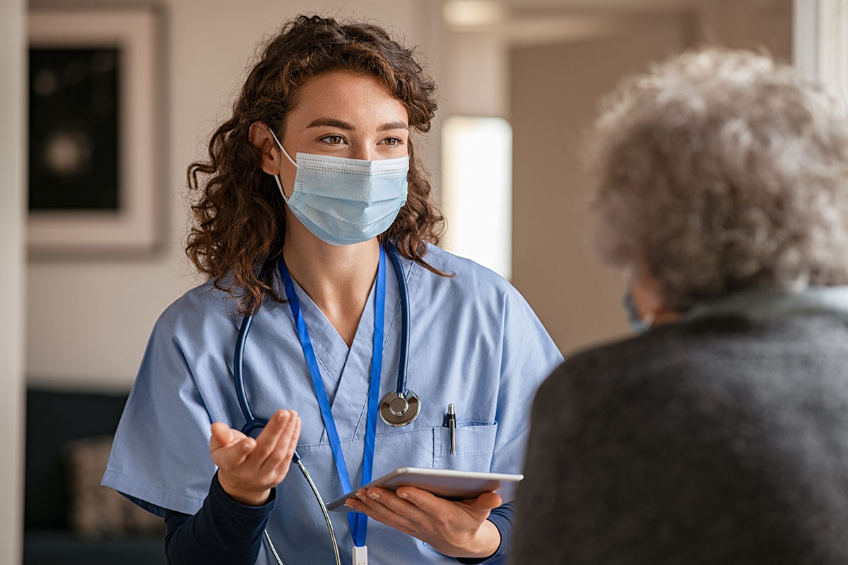 A female health care worker wearing a face mask speaks to a patient