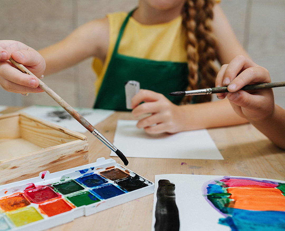 A child sits at a table with paint and paper